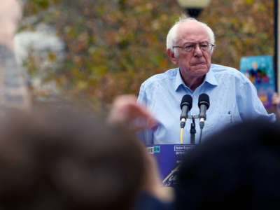 A damp Bernie Sanders speaks at a podium in the rain during an event