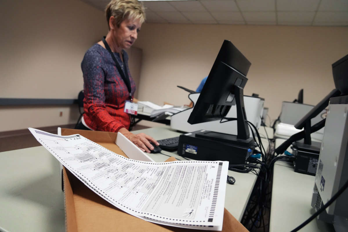 A woman works on a computer as ballots are seen in a box near her