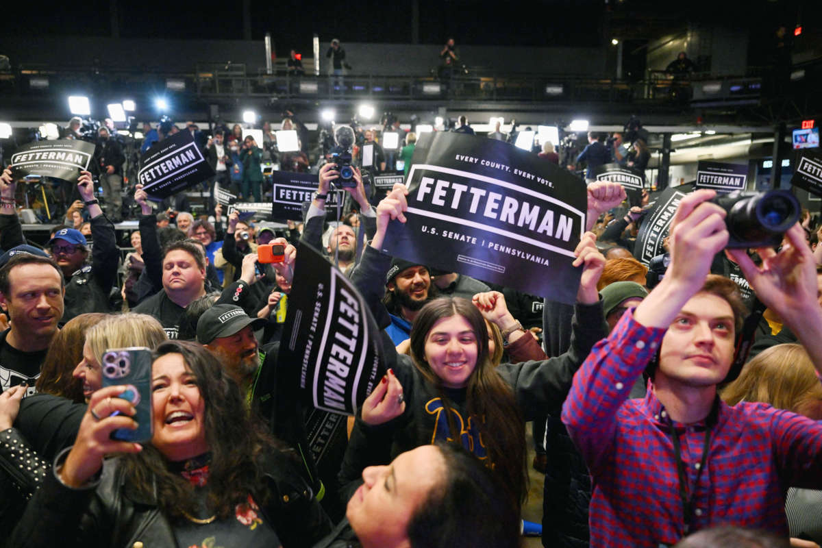 A crowd of John Fetterman supporters wave his banners in the air in celebration of his electoral victory