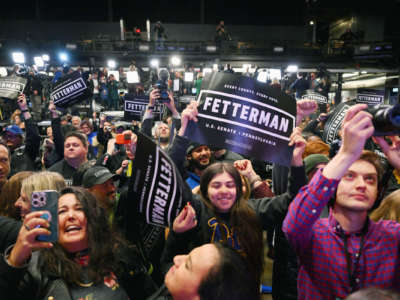 A crowd of John Fetterman supporters wave his banners in the air in celebration of his electoral victory