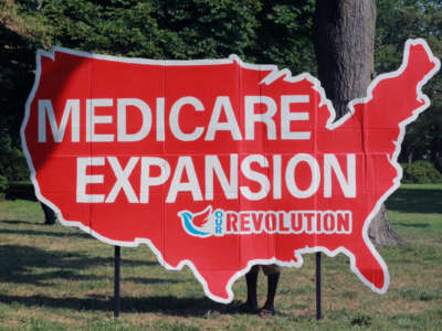 A cardboard sign in the shape of the contiguous continental United States reads "MEDICARE EXPANSION" with the "Our Revolution" logo beneath it