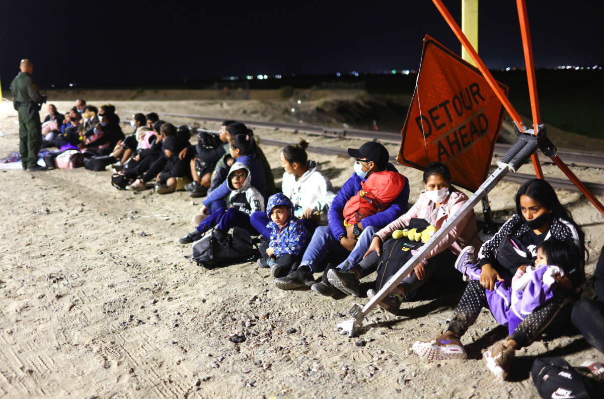 Immigrants wait in the early morning hours to be processed by the U.S. Border Patrol after crossing from Mexico, with the U.S.-Mexico border barrier in the background, on May 23, 2022, in Yuma, Arizona.