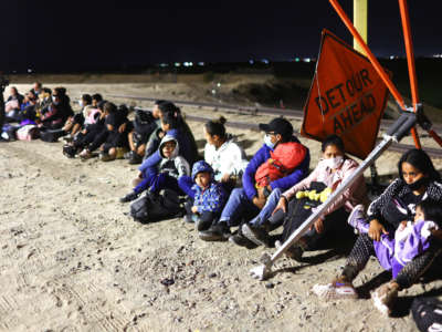 Immigrants wait in the early morning hours to be processed by the U.S. Border Patrol after crossing from Mexico, with the U.S.-Mexico border barrier in the background, on May 23, 2022, in Yuma, Arizona.