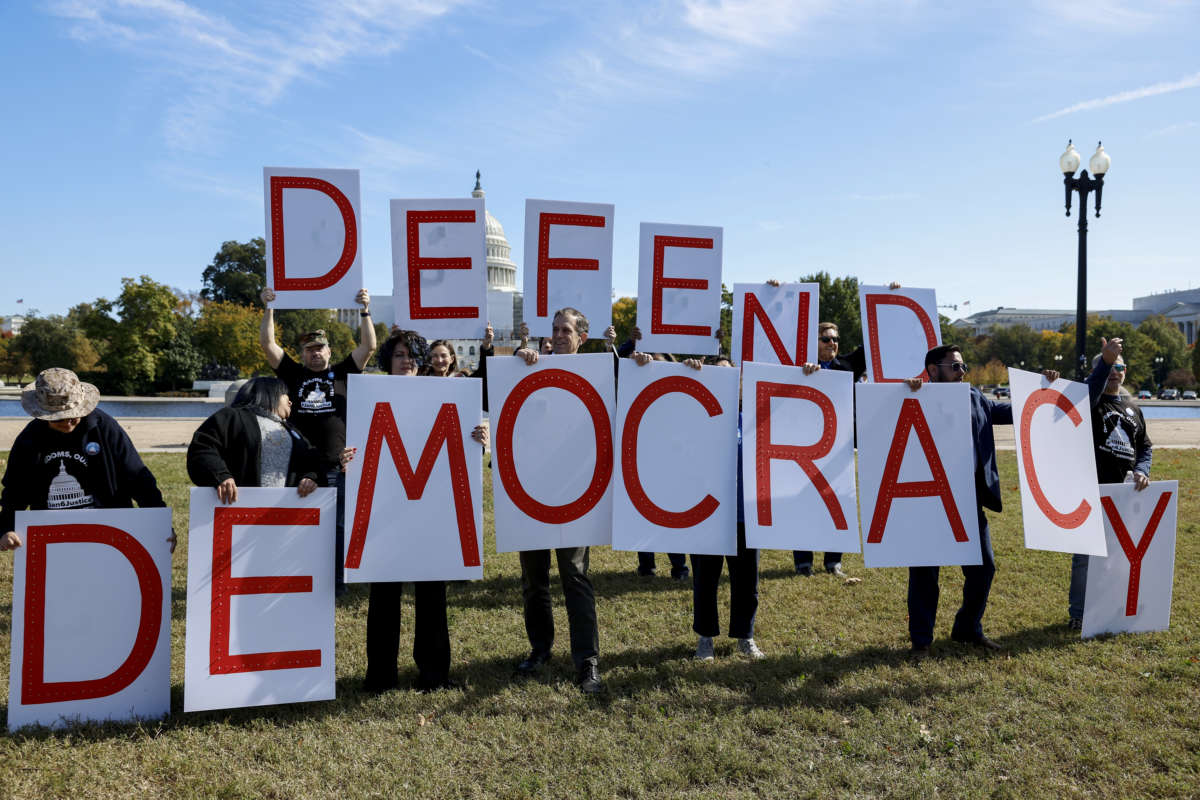Activists with Our Revolution hold up signs spelling out "Defend Democracy" while calling for accountability for the January 6 attack on the U.S. Capitol building on the National Mall on October 20, 2022, in Washington, D.C.