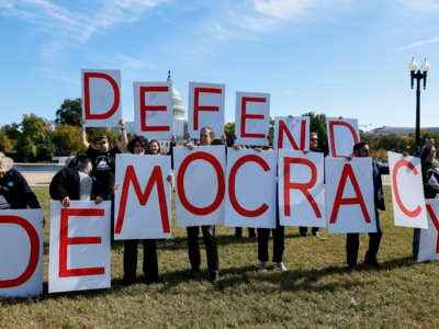 Activists with Our Revolution hold up signs spelling out "Defend Democracy" while calling for accountability for the January 6 attack on the U.S. Capitol building on the National Mall on October 20, 2022, in Washington, D.C.