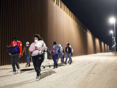 Immigrants walk along the U.S.-Mexico border barrier in the early morning hours on their way to be processed by the U.S. Border Patrol after crossing from Mexico, on May 23, 2022, in Yuma, Arizona.