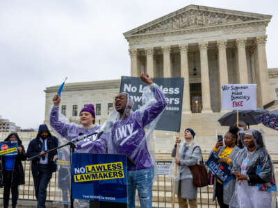 Jessica Rohloff and Demetrius Fisher of League of Women Voters cheer on the crowd as demonstrators protest during a rally at the Supreme Court during oral arguments in Moore v. Harper on December 7, 2022, in Washington, D.C.