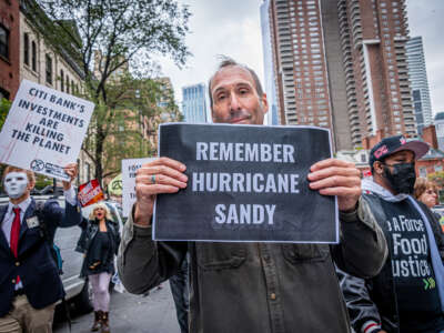 A protester holds a sign reading "REMEMBER HURRICANE SANDY" during an outdoor protest