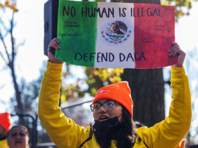 A protester chants while holding a sign fashioned after the Mexican flag that reads: NO HUMAN IS ILLEGAL; DEFEND DACA