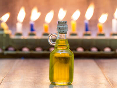 A lit menorah is seen behind an in-focus bottle of oil