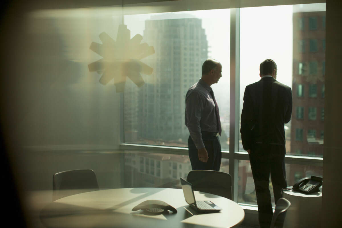 Two businessmen look down from highrise office window