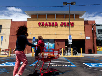 Woman with kid sitting on shopping cart in front of Trader Joe's in California.