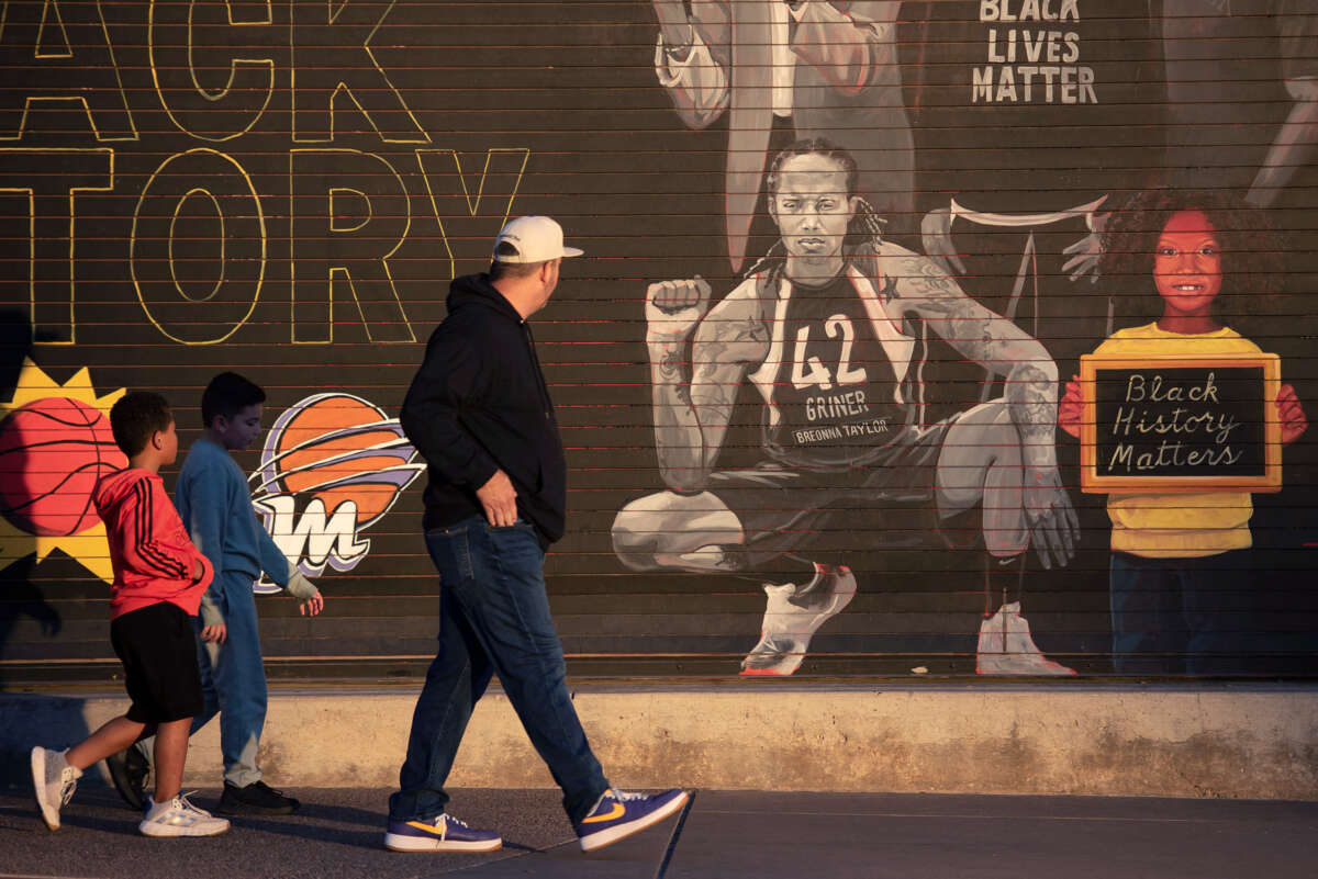 A man and two boys look at a mural featuring Brittney Griner