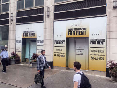 People walk by an ad for a rental retail space on a city street