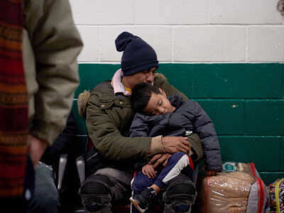 A man holds his sleeping son as they wait in a bus station