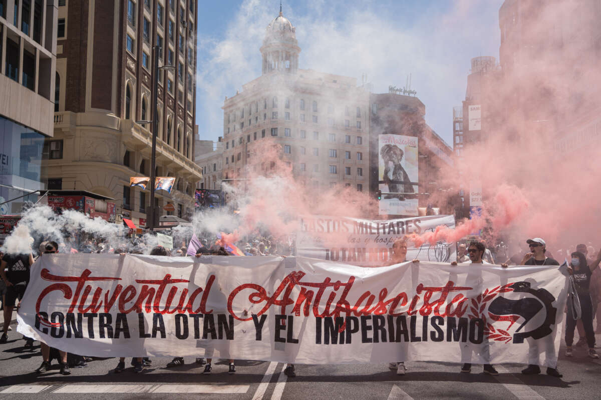 Anti-fascist protesters hold a banner and red smoke flares during a demonstration against NATO in Madrid, Spain on June 26, 2022.