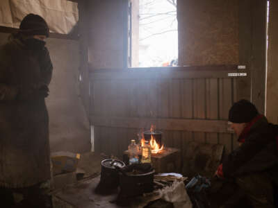 Two women dressed for the cold prepare lunch over a fire next to an open window