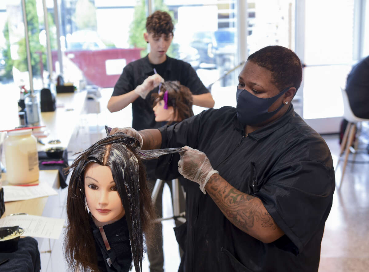 Students Tyneisha Bell, front, and Chelsea Wheeler, practice a color application on mannequin heads at the American Barber and Beauty Academy in Reading, Pennsylvania on June 15, 2021.