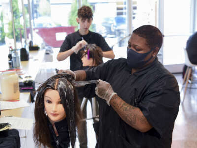 Students Tyneisha Bell, front, and Chelsea Wheeler, practice a color application on mannequin heads at the American Barber and Beauty Academy in Reading, Pennsylvania on June 15, 2021.