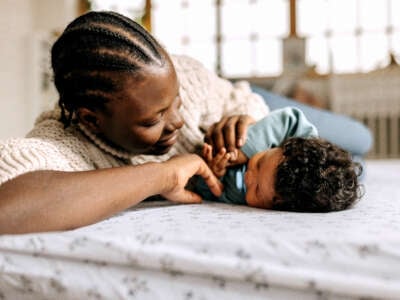 A Black mother lays down with her baby in a bedroom