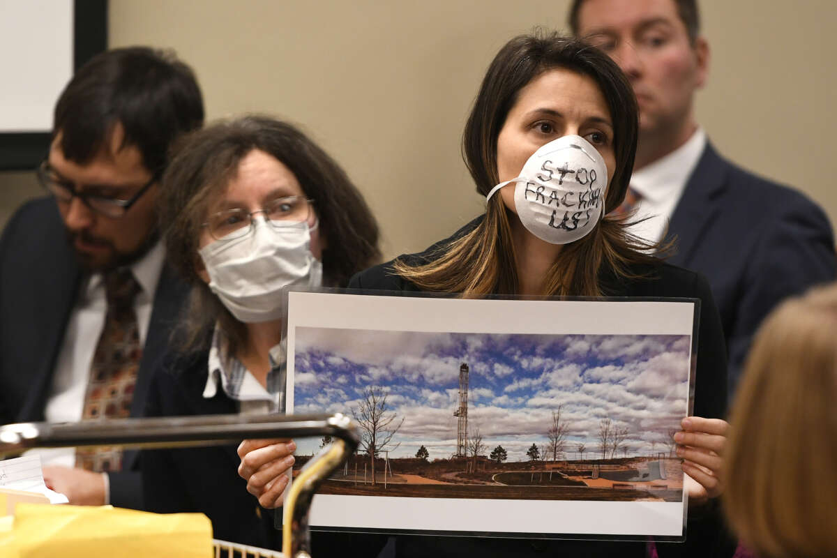 Lauren Petrie, of Food & Water Watch, holds up a photo of a fracking site near a playground and wears a mask to show opposition to Colorado Oil and Gas Conservation Commission (COGCC) board members during a public comment session on October 30, 2017 in Denver, Colorado.