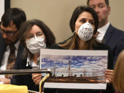 Lauren Petrie, of Food & Water Watch, holds up a photo of a fracking site near a playground and wears a mask to show opposition to Colorado Oil and Gas Conservation Commission (COGCC) board members during a public comment session on October 30, 2017 in Denver, Colorado.