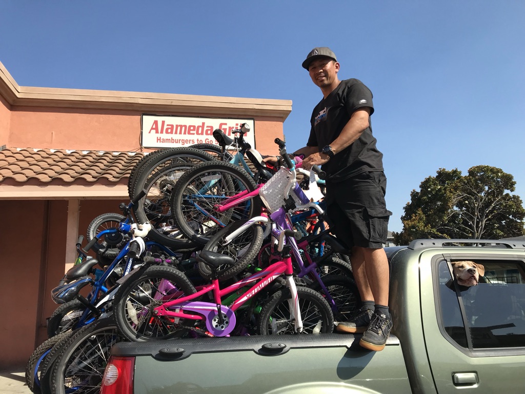 A man stands on the back of a pickup truck filled with repaired bicycles