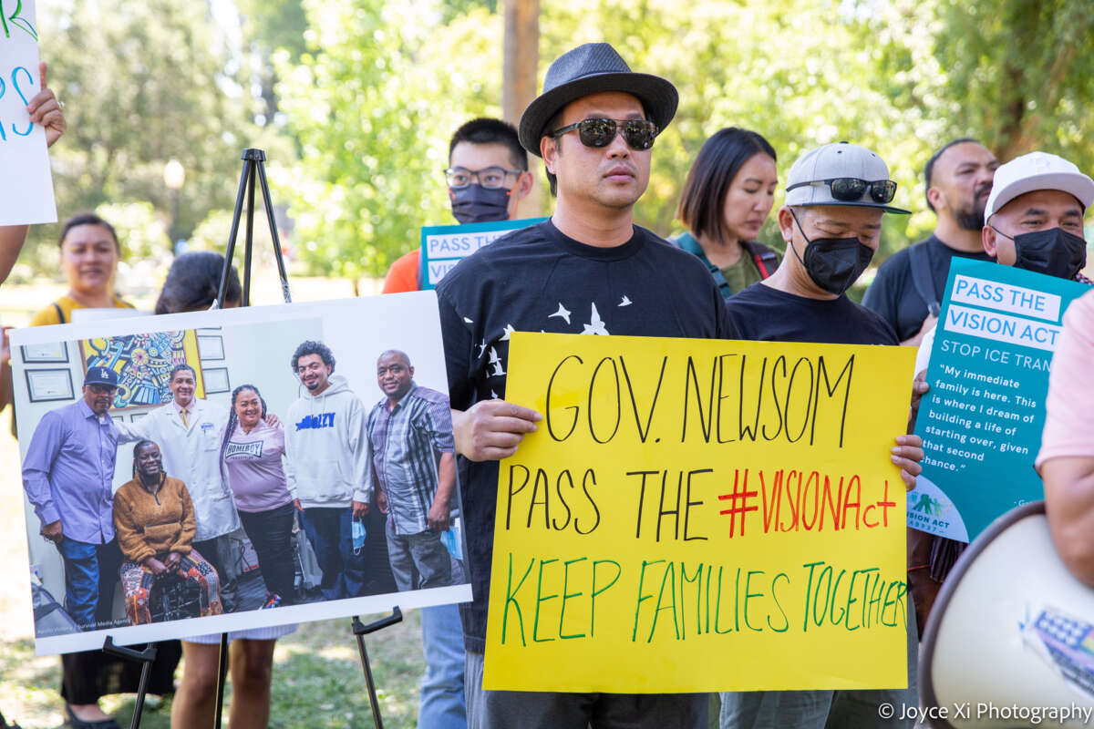 A man holds a sign reading "GOV. NEWSOM: PASS THE #VISIONACT; KEEP FAMILIES TOGETHER during an outdoor protest