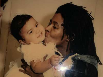 A photo showing a woman holding a kissing the cheek of an infant