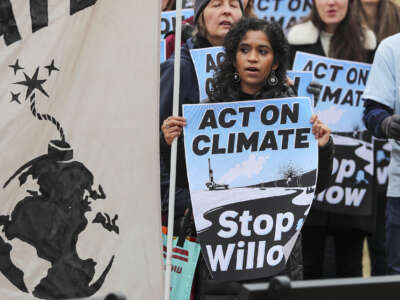 an activist holding a sign reading "ACT ON CLIMATE; STOP WILLOW" stands with others during an outdoor protest