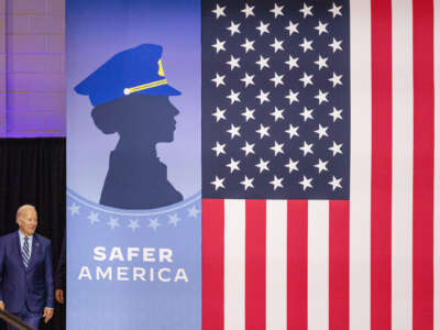 Joseph Robinette Biden emerges from behind a banner bearing the silhouette of a cop and the words "SAFER AMERICA"