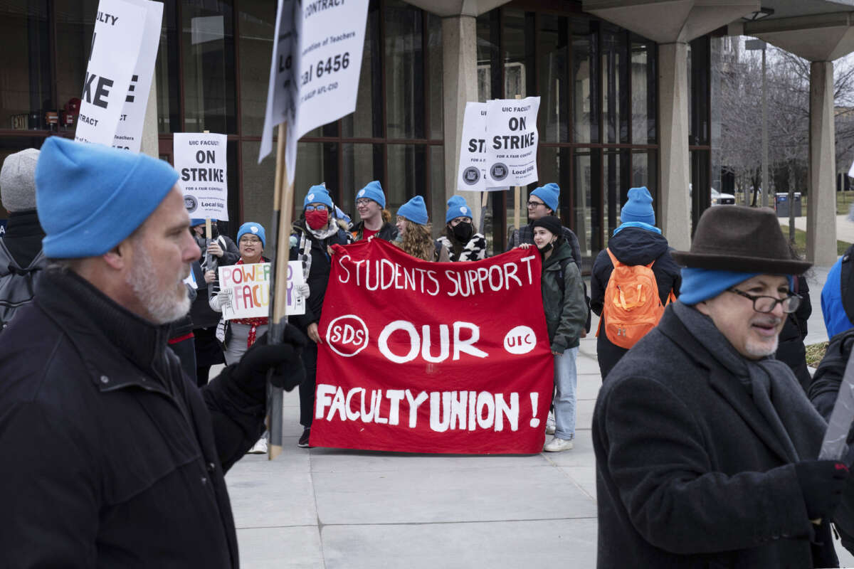 People hold a red banner reading "STUDENTS SUPPORT OUR FACULTY" as striking professors protest around them