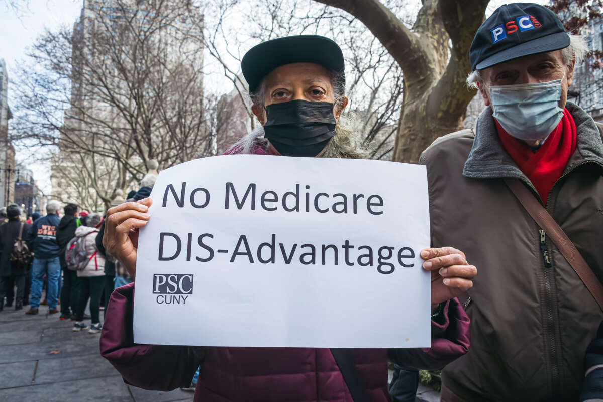 A person in a mask holds a sign reading "No Medicare DIS-Advantage" while participating in an outdoor protest