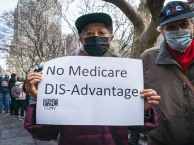 A person in a mask holds a sign reading "No Medicare DIS-Advantage" while participating in an outdoor protest