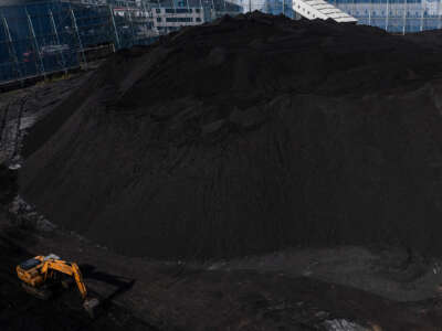 A backhoe is seen next to a towering hill of coal