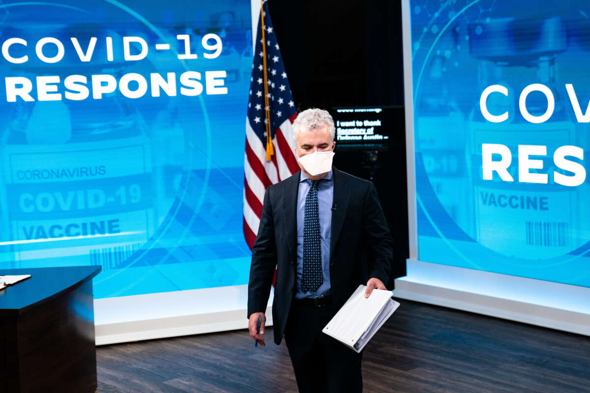 Jeff Zients holds a document while standing in in front of screens reading "COVID-19 RESPONSE"