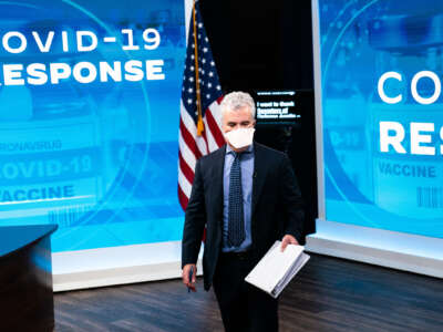 Jeff Zients holds a document while standing in in front of screens reading "COVID-19 RESPONSE"