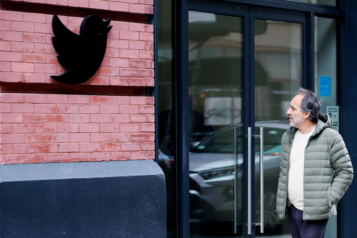 A man walks past Twitter's headquarters while staring at the black Twitter logo affixed to the wall