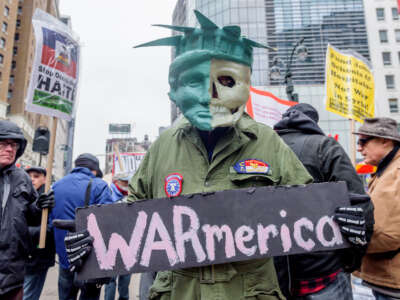 A protester is holding a sign that reads "WARmerica" and is dressed in a jumpsuit and a mask with half the face modeled on the statue of liberty and half the face a skull. Hundreds took to the streets as antiwar and social justice groups organized a demonstration against the US bombing of Syria and opposing endless U.S. wars on April 15, 2018, in New York City.