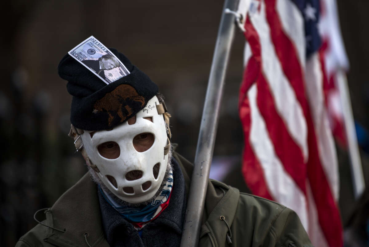 A man wearing a hockey mask and a hat with a dollar bill imprinted with Donald Trump looks on as protesters rally outside the governor's mansion on December 5, 2020 in St. Paul, Minnesota.