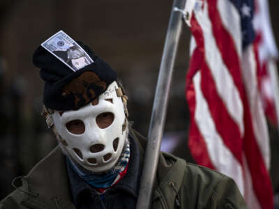 A man wearing a hockey mask and a hat with a dollar bill imprinted with Donald Trump looks on as protesters rally outside the governor's mansion on December 5, 2020 in St. Paul, Minnesota.