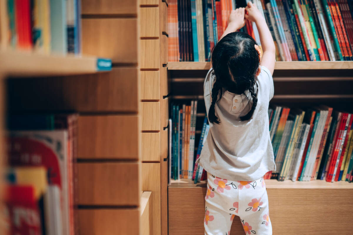 Little girl getting book off a book shelf in a library