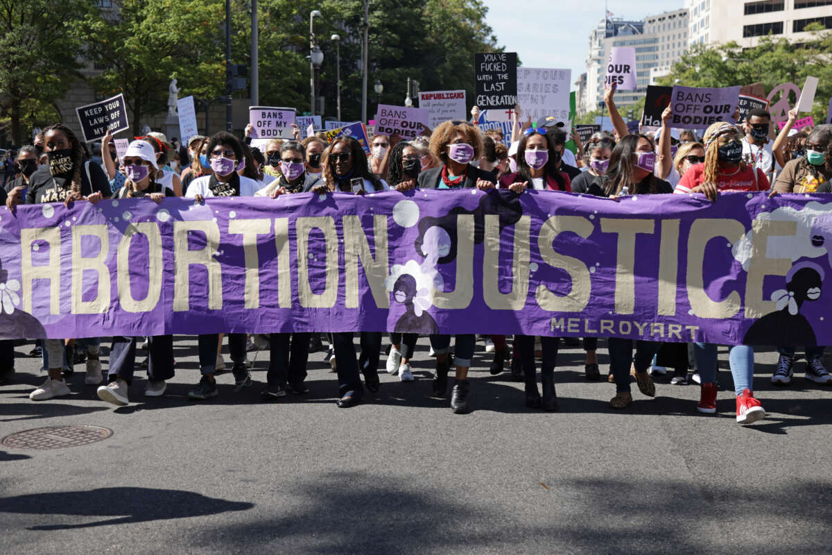A diverse group of activists holds a purple banner saying "Abortion Justice" in Washington DC