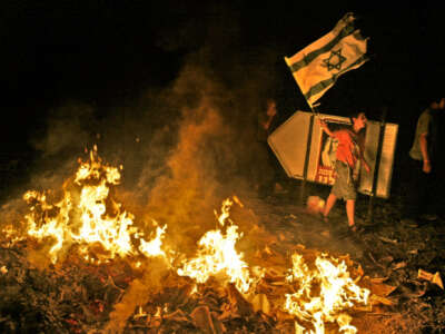 A Jewish protestor waves the Israeli flag next to a bonfire started by a mob who looted the back of a passing vehicle loaded with maps of the Gaza Strip in front of the Neve Dekalim settlement in the Gaza Strip on August 14, 2005.
