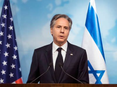 Antony Blinken stands in front of U.S. and Israeli flags while delivering a speech