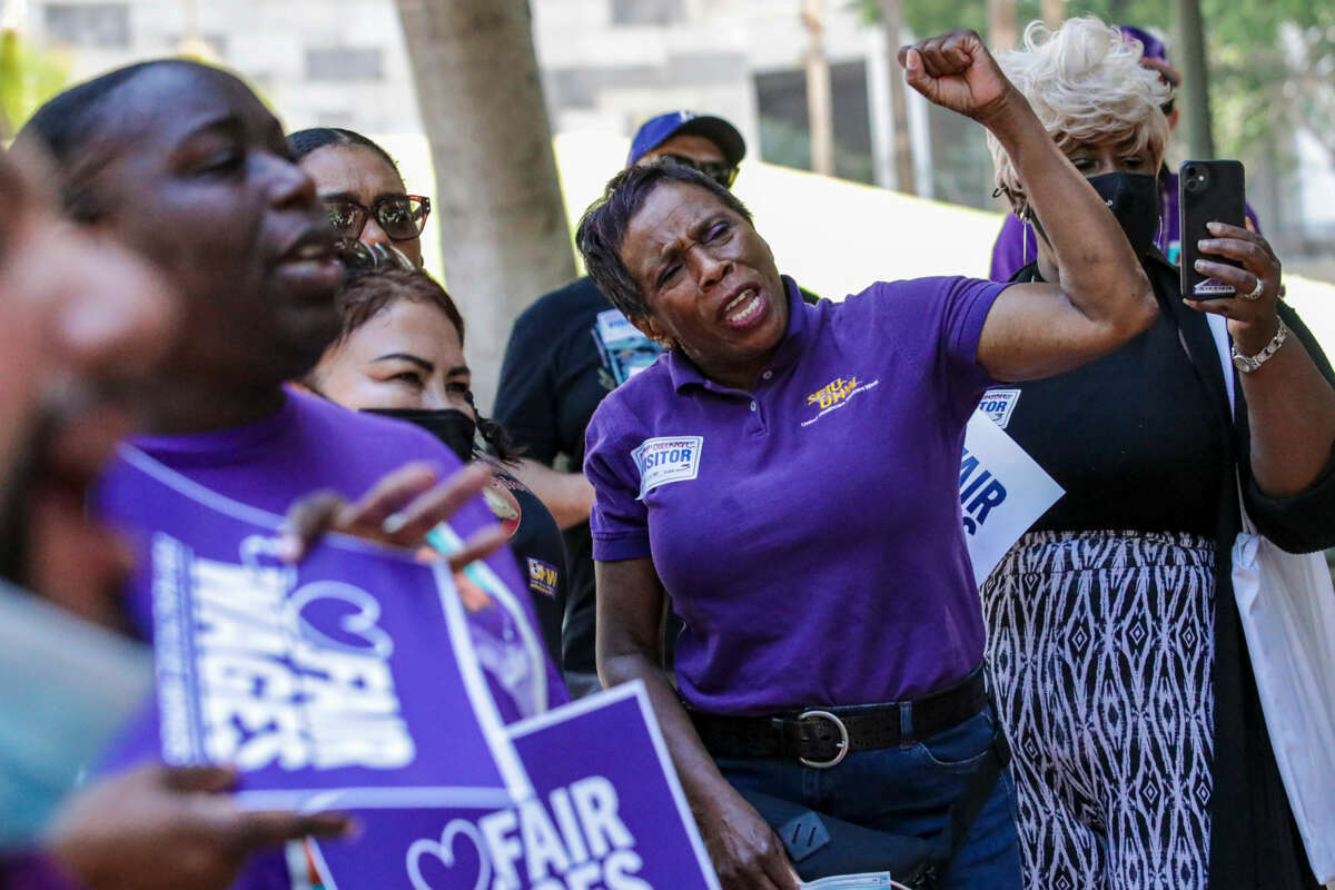A woman in purple pumps her fist in celebration while surrounded by other medical workers, also wearing purple, during an outdoor rally