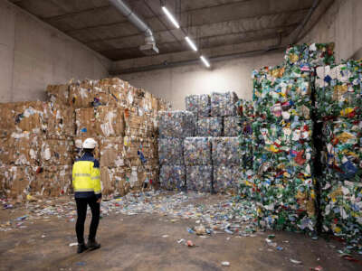 A woker stares at towering piles of compacted plastic refuse in a recycling facility