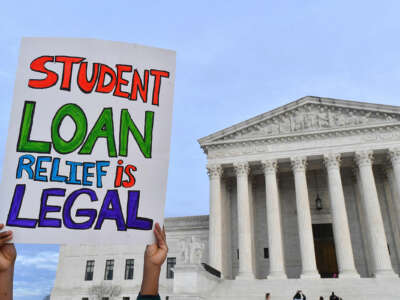 A protester holds up a sign reading "STUDENT LOAN RELIEF IS LEGAL" outside of the United States Supreme Court building