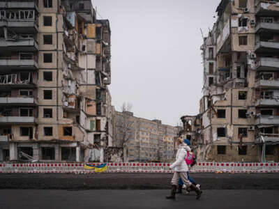 People walk by the rubble of partially-destroyed apartment buildings