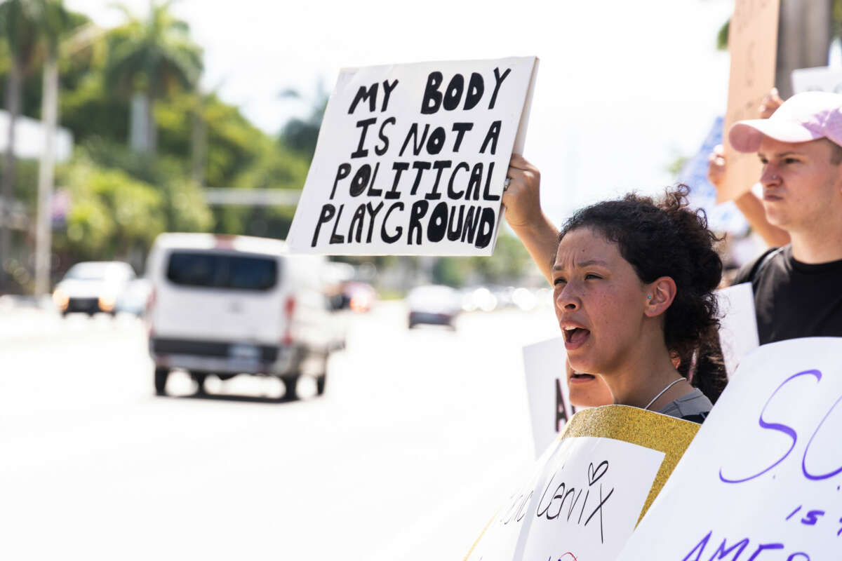 A person holds a sign reading "MY BODY IS NOT A POLITICAL PLAYGROUND" during a roadside protest